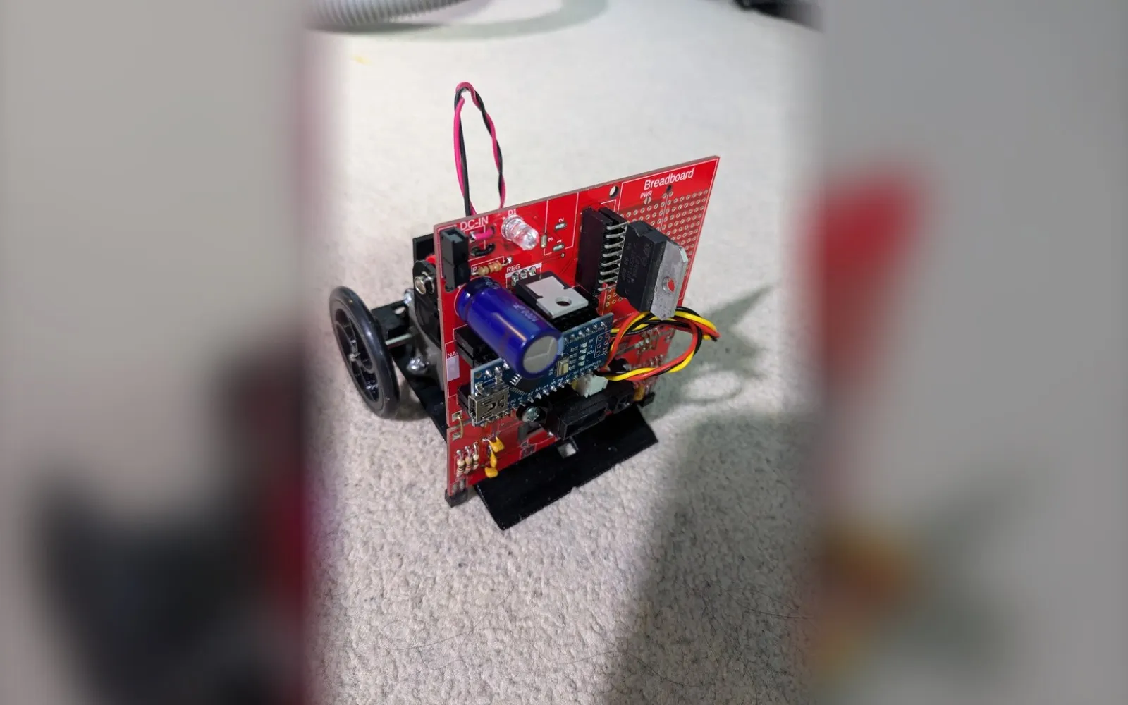 Assembled sumo robot with a red PCB, Arduino Nano, large capacitor, black chassis, and rubber wheels.